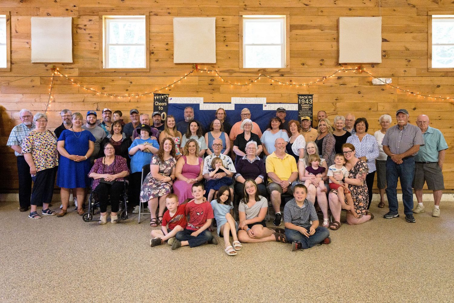 Group photo of people gathered in a rustic wood-paneled room with windows.
