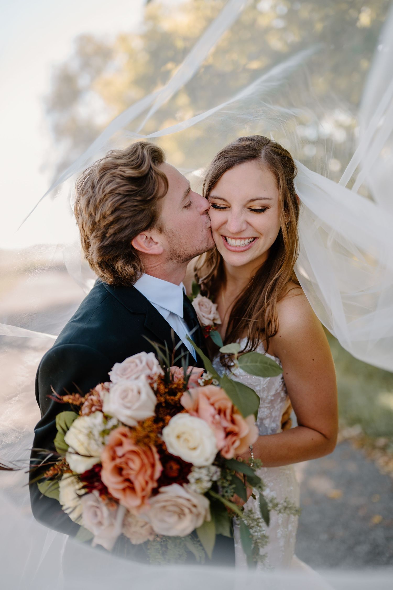 A romantic wedding couple in white attire share an intimate moment on a modern terrace with cityscape views.