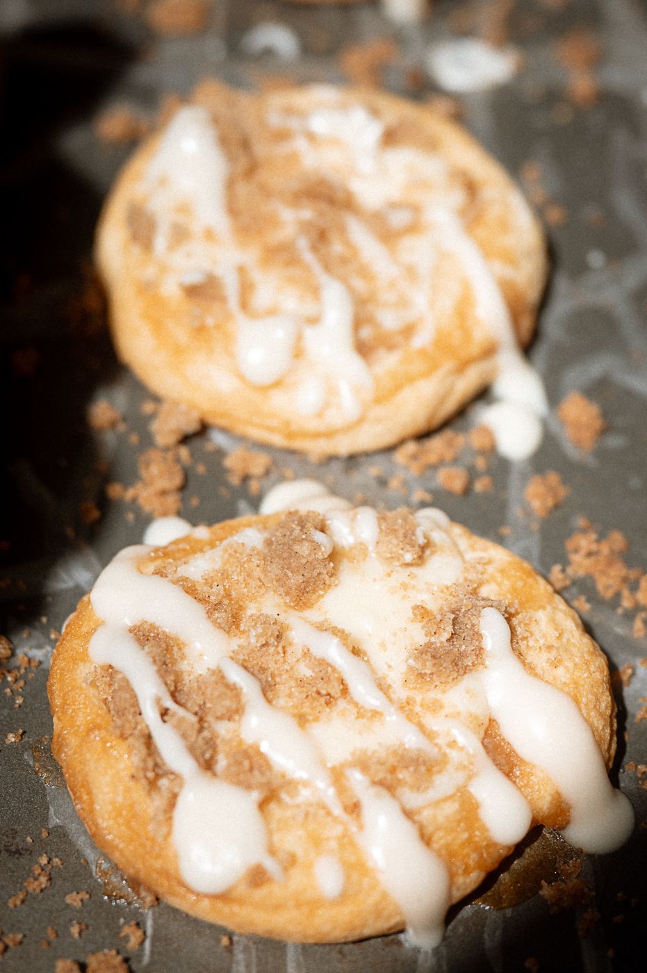 Freshly baked snickerdoodle cookies drizzled with sweet white glaze on a dark baking sheet.