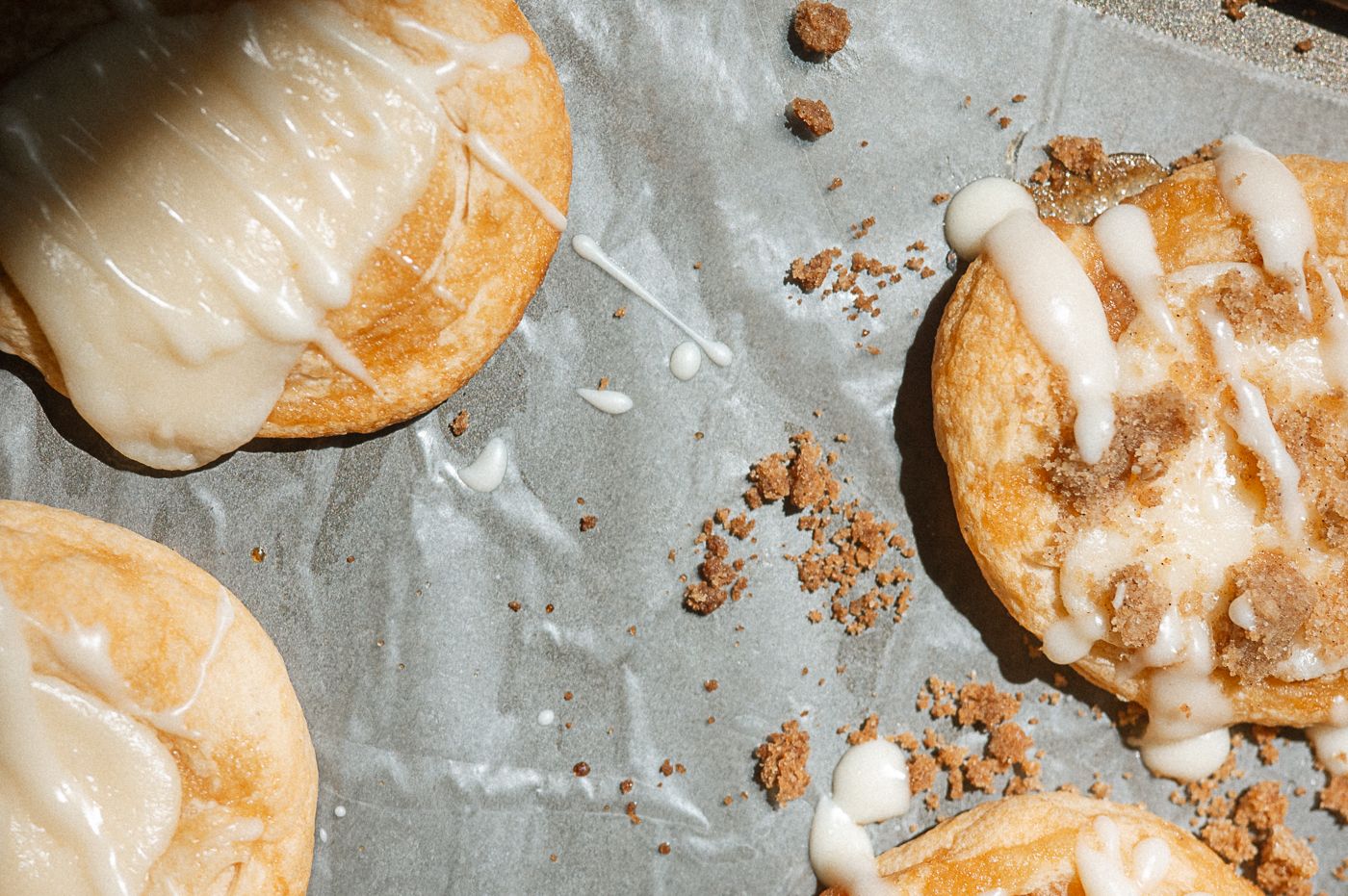 Freshly baked cream puffs drizzled with white glaze arranged in a row on a baking sheet.