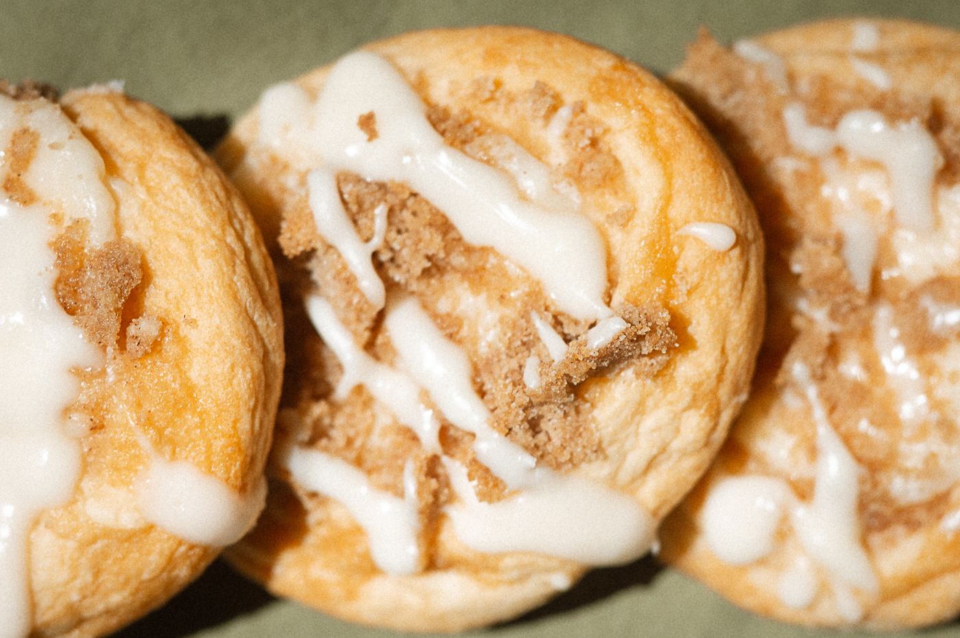 Golden brown cream puffs with vanilla icing lined up on a rustic metal surface.