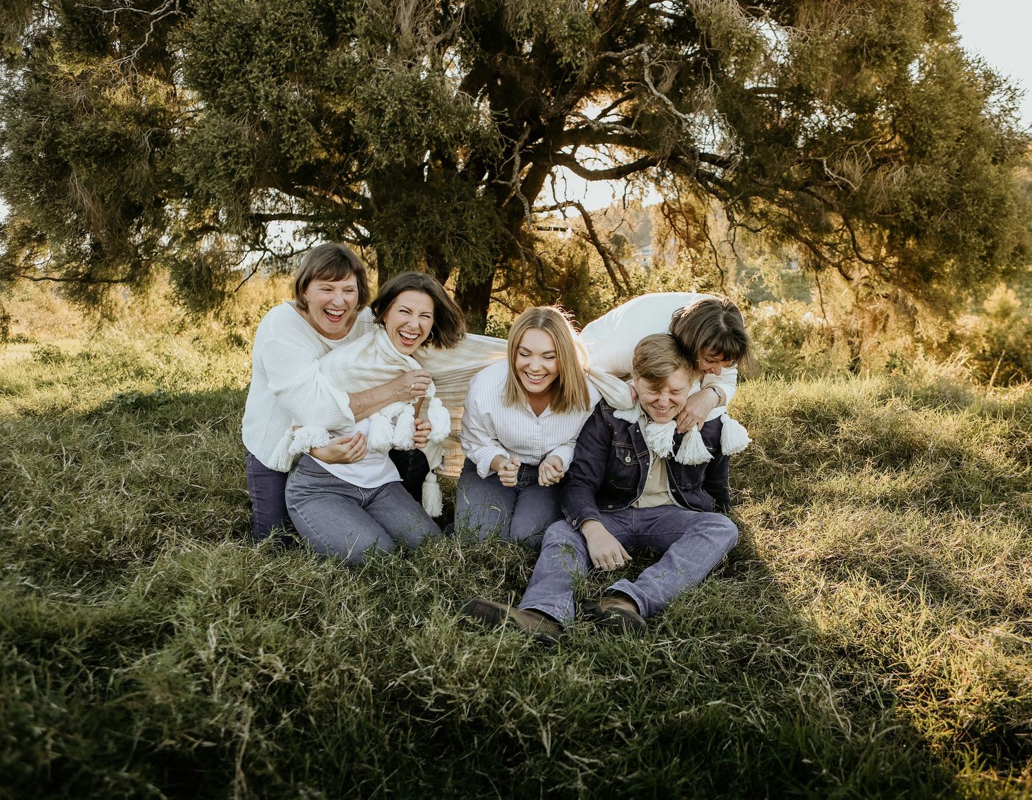 People sitting together on grassy hillside during golden hour with trees in the background.