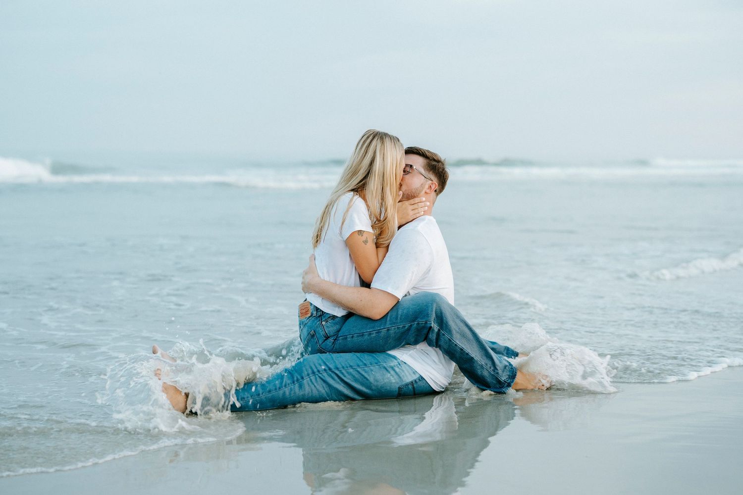 A playful couple relaxing in the shallow ocean waves at the beach during golden hour.
