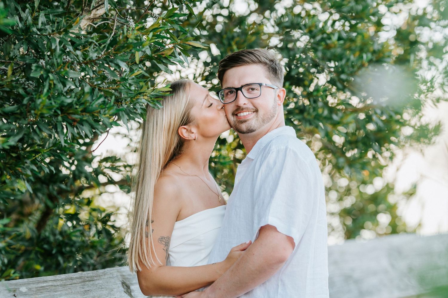 Romantic couple embracing outdoors with sunlight peeking through trees in the background.