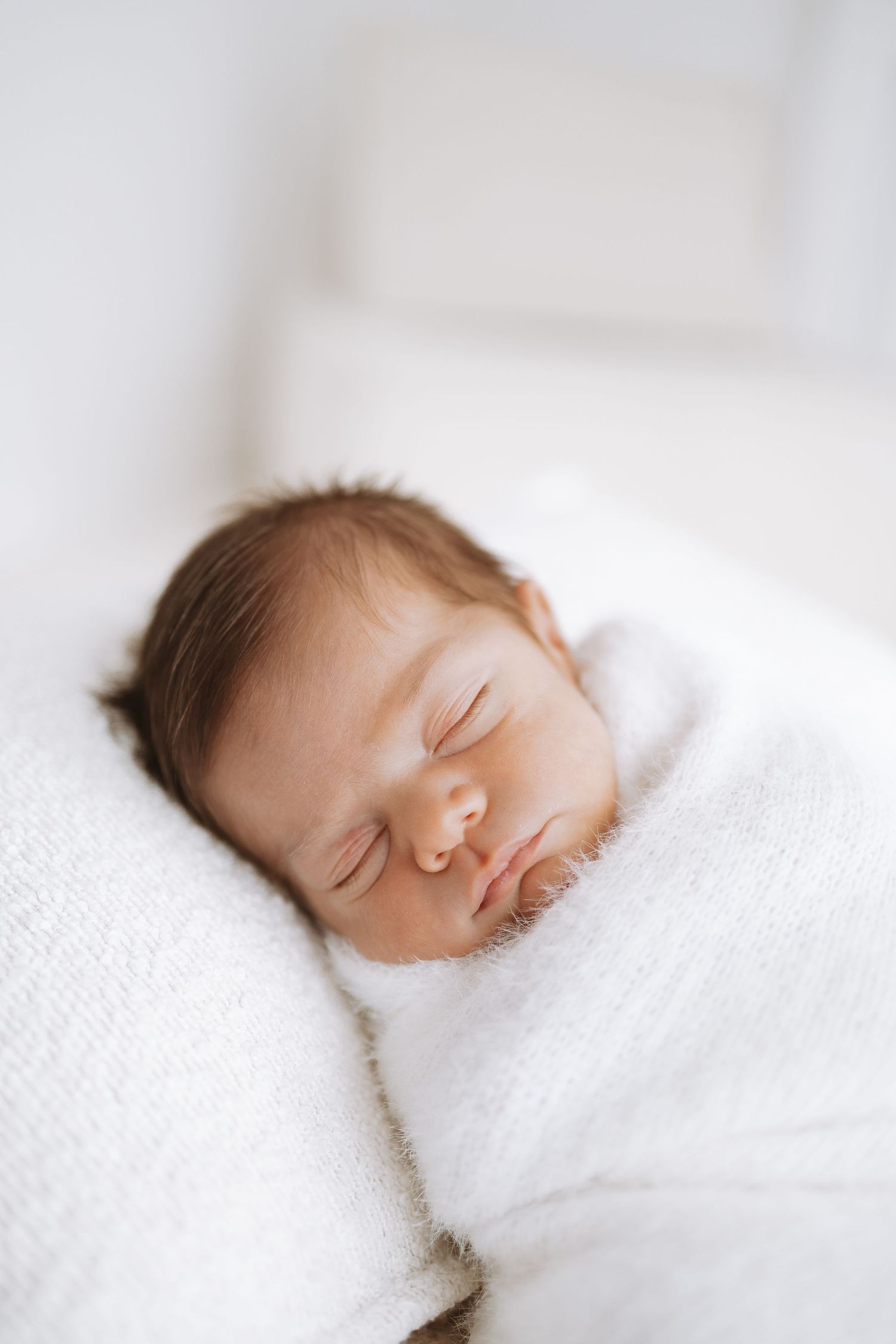 Peaceful newborn baby sleeping soundly on white textured bedding in soft natural light.