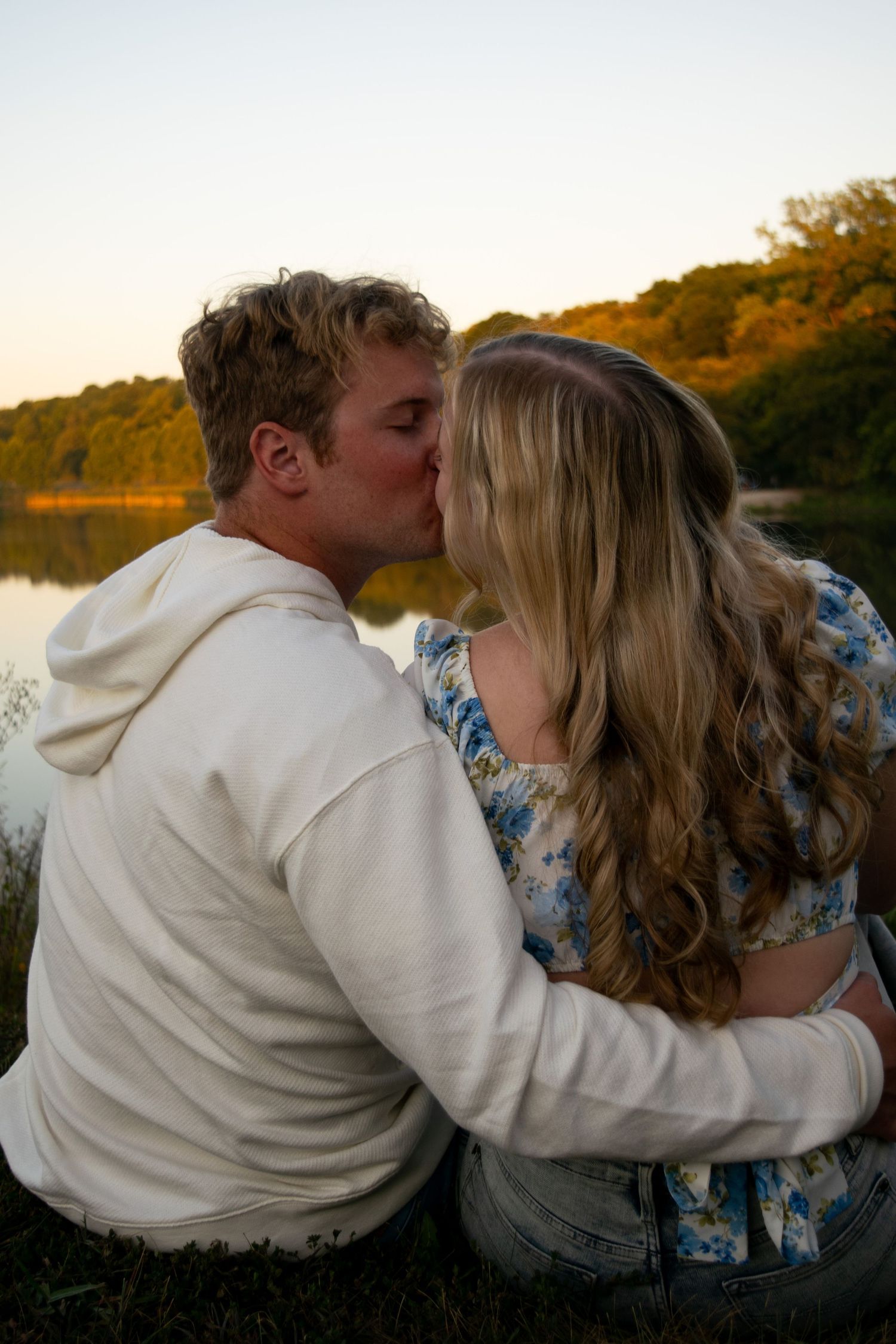 Couple sitting on the ground in front of a lake kissing