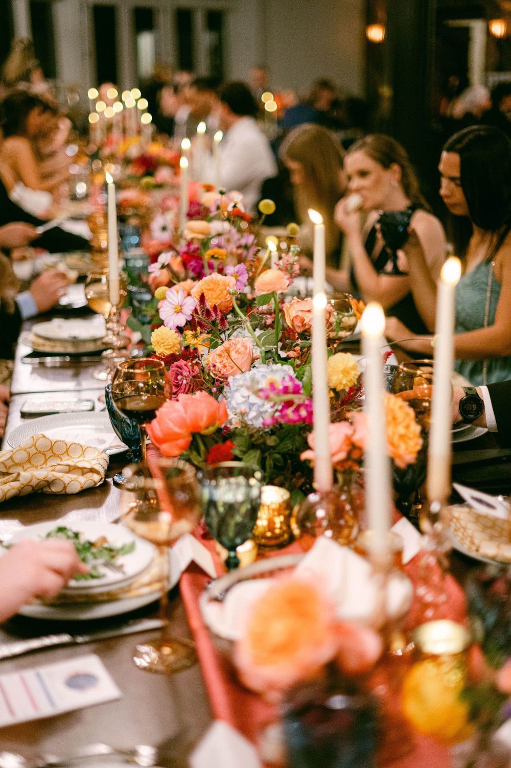 Elegant dinner table setting with pink flowers, lit candles and fine china plates at a dimly lit event gathering.
