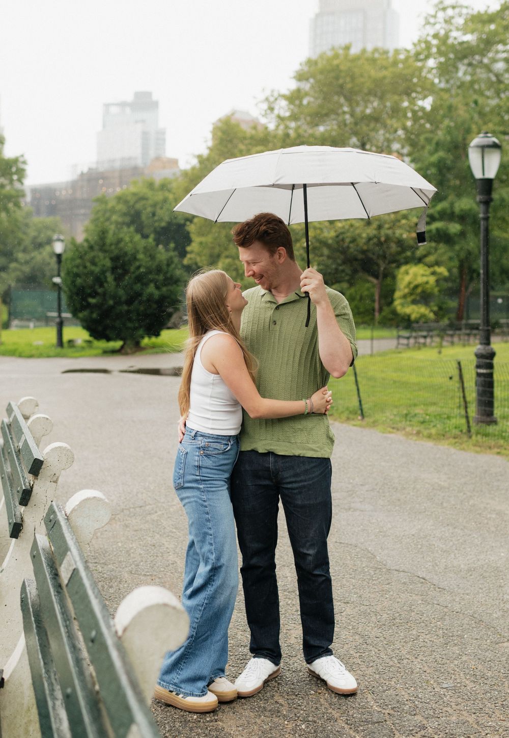 A couple walks together under a white umbrella along a park path on an overcast day.
