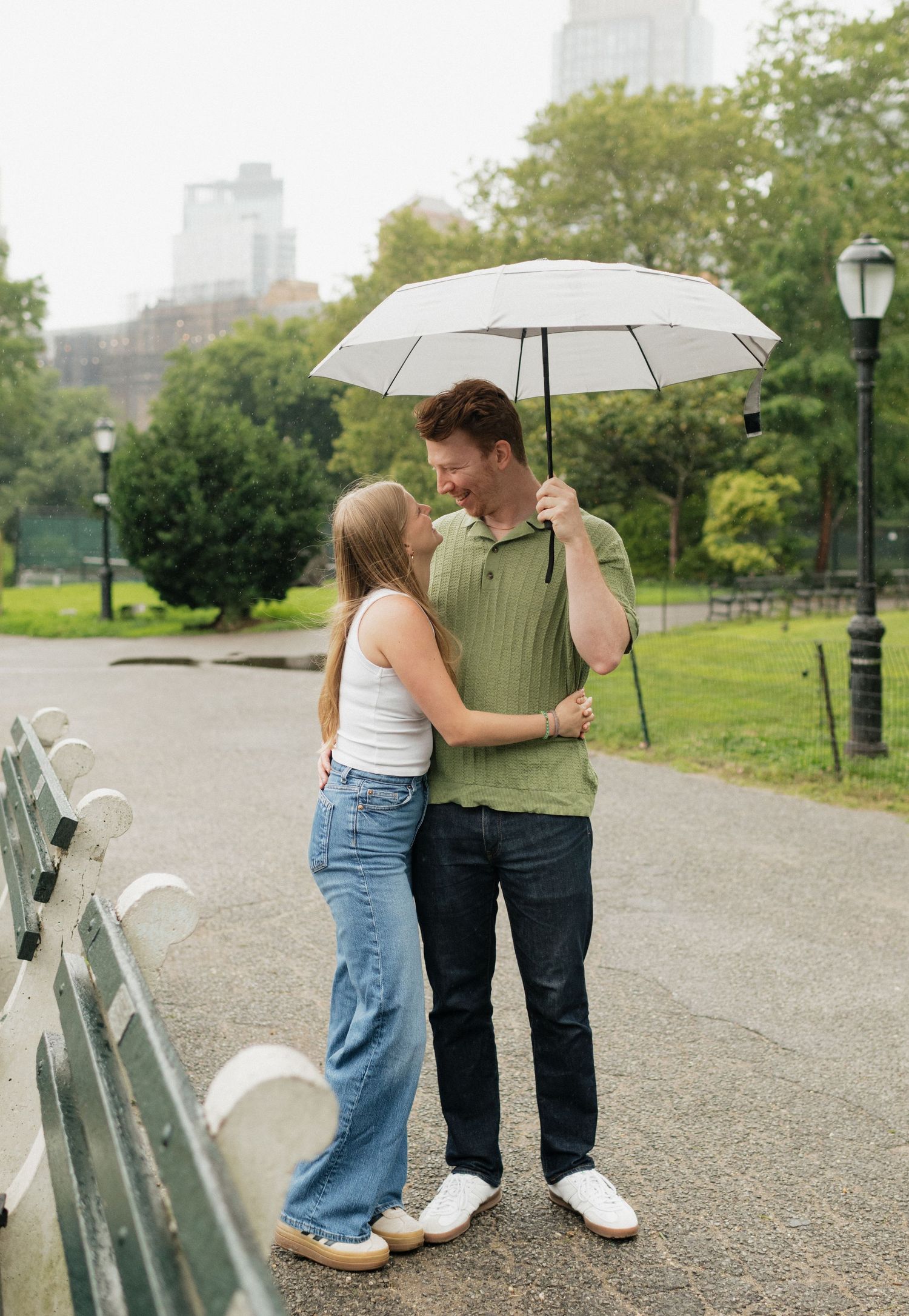 A couple walks together under a white umbrella along a park path on an overcast day.
