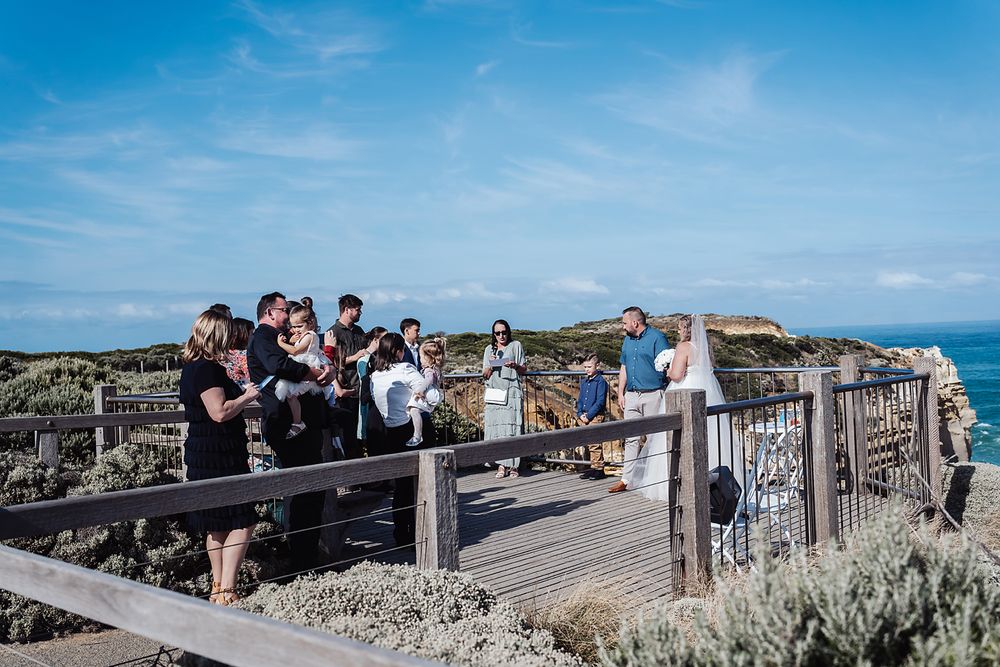 People gather on an ocean-view platform overlooking coastal cliffs and water on a bright sunny day.