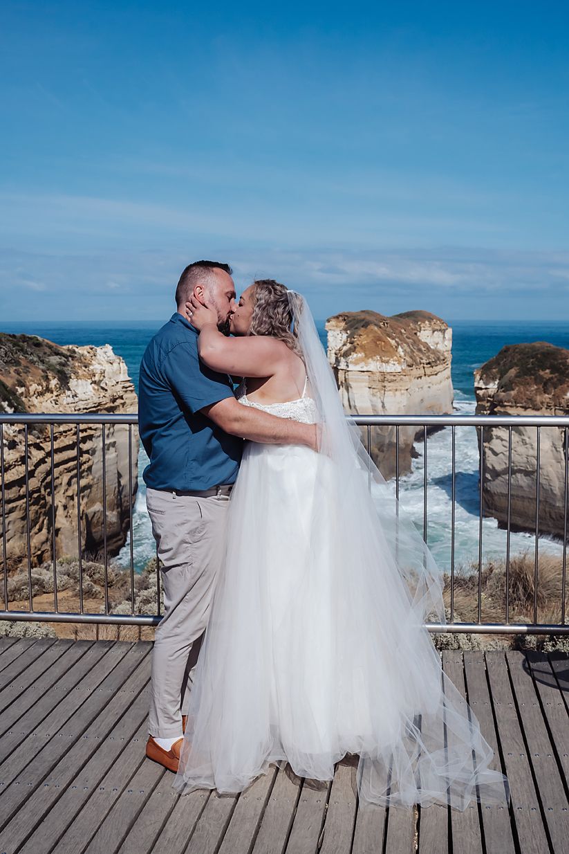 Newlyweds share an intimate moment on a wooden boardwalk overlooking dramatic coastal cliffs and ocean views.