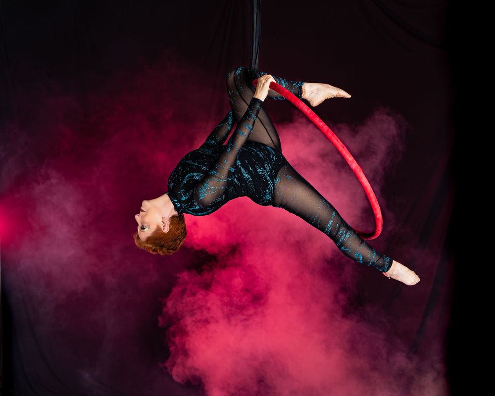 Dramatic sequence of aerial dance movements against pink and purple atmospheric fog with black mesh costume.