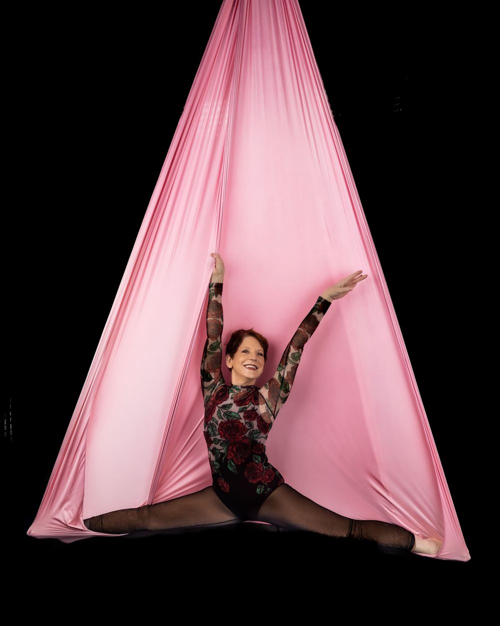 A performer gracefully moves within flowing pink aerial silks against a dark background in a series of dynamic poses.
