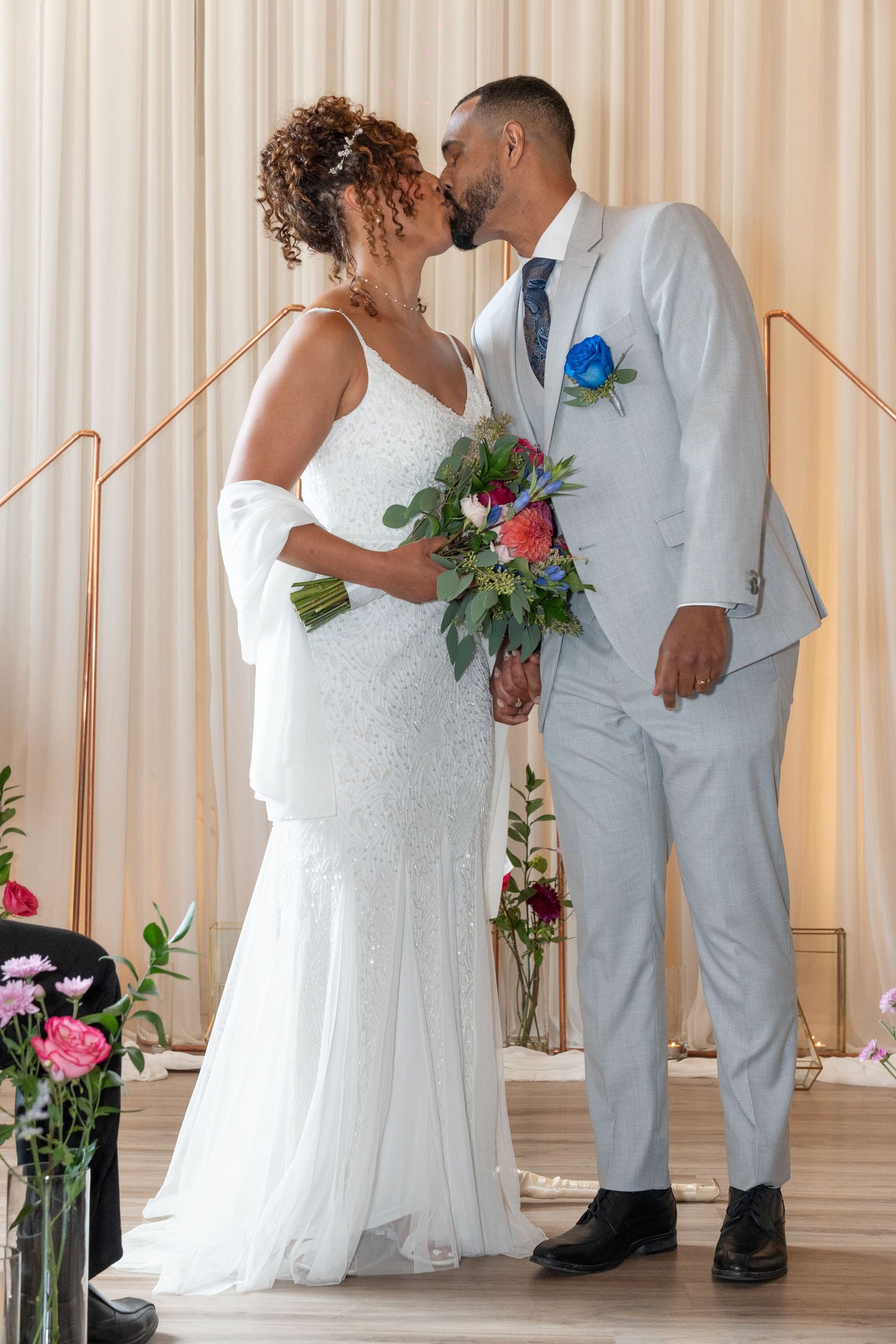 Multiple romantic wedding couples share sweet kisses while wearing elegant white dresses and suits against a cream backdrop.