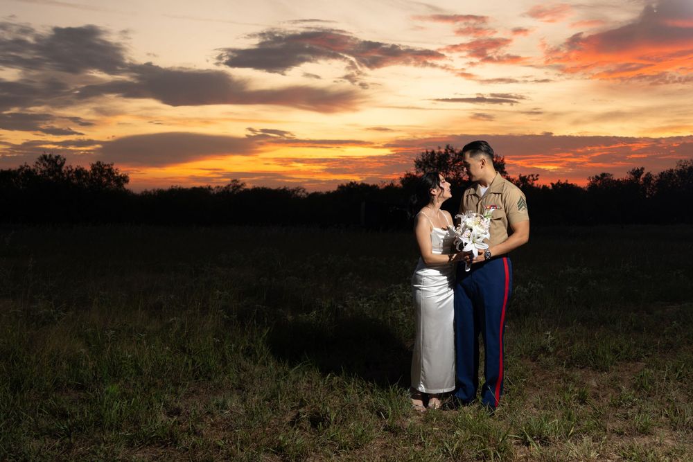 Silhouetted figures embrace on a hill against a dramatic orange and purple sunset sky during a photo session.
