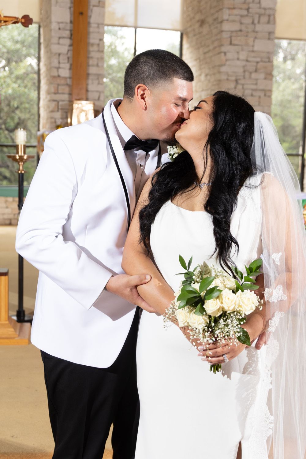A wedding couple poses for romantic photos against a stone wall backdrop with soft lighting.