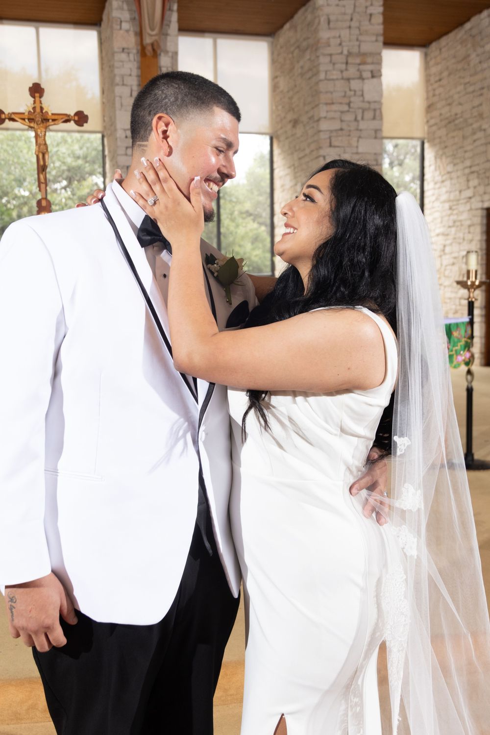 A joyful moment between newlyweds sharing a laugh inside a church with stone walls and crosses visible in background.