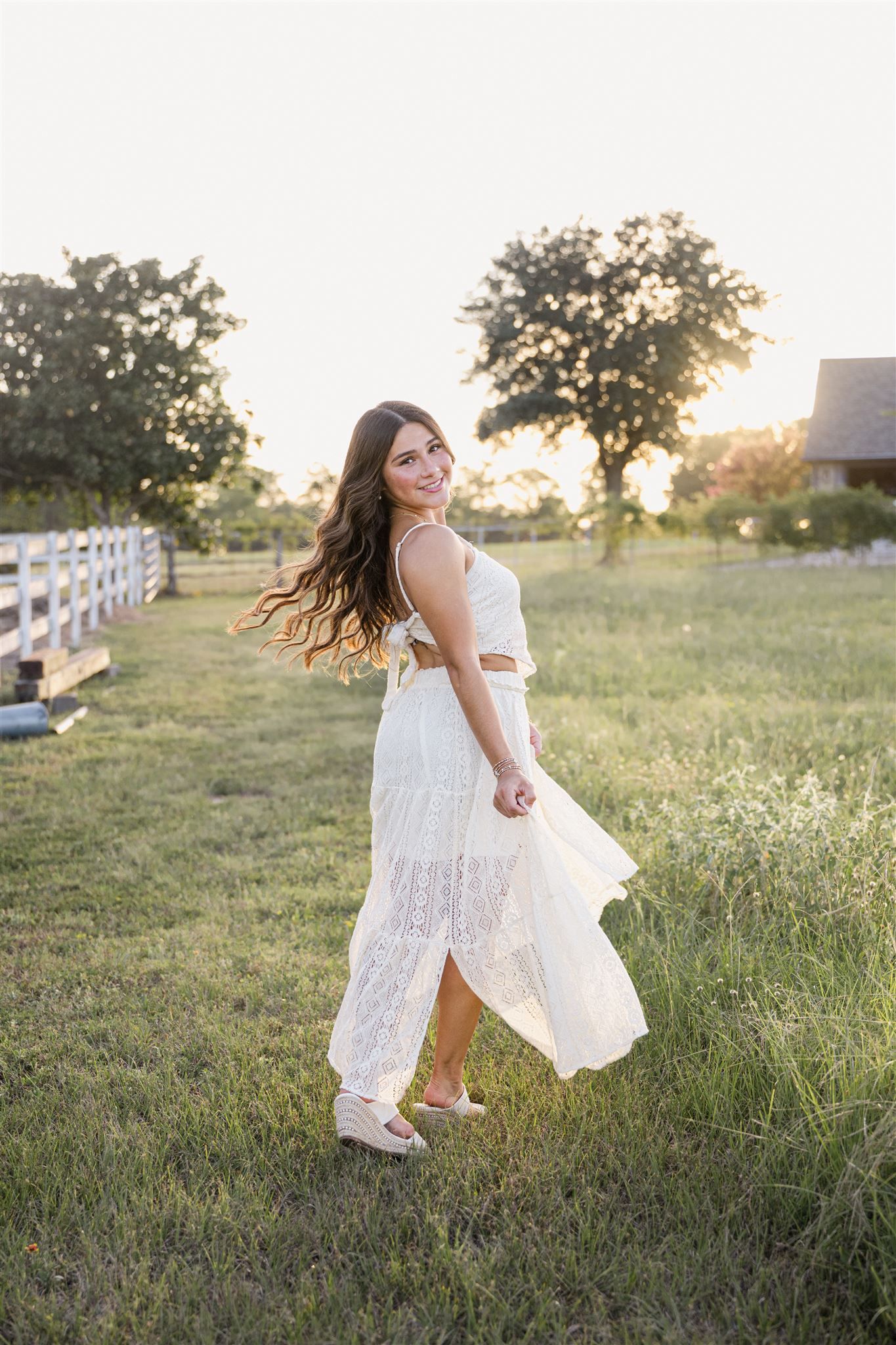 Ethereal scene of a girl with long wavy brunette hair in a flowy white dress twirling in a sunlit meadow at golden hour.