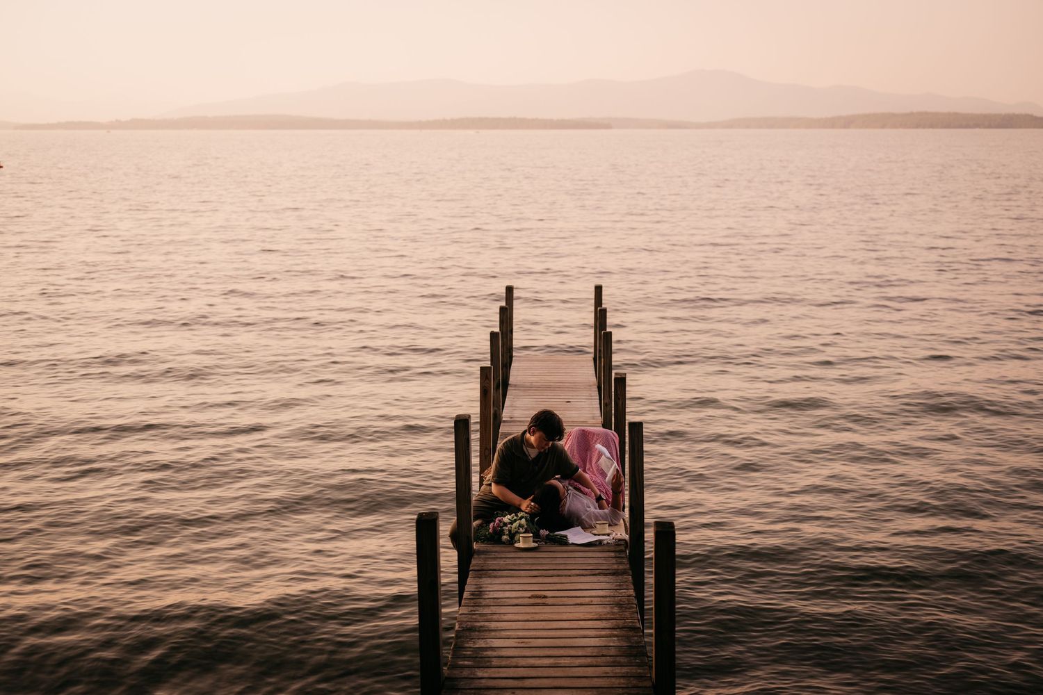 Couple sitting together on a wooden dock over calm water at sunset.