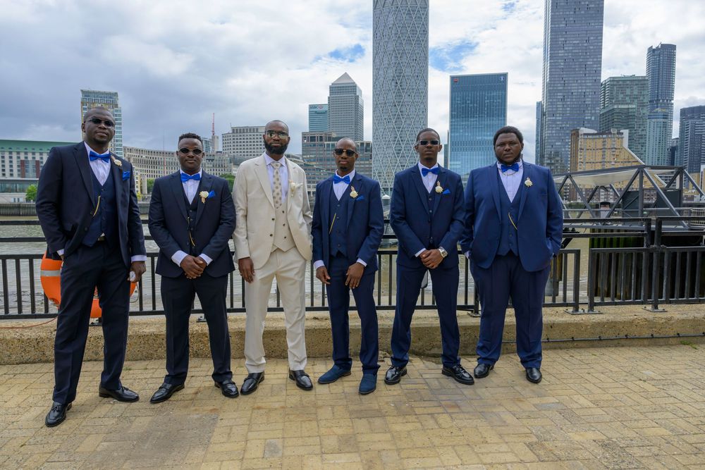 A formal group in suits pose together on a rooftop with city skyscrapers in the background.