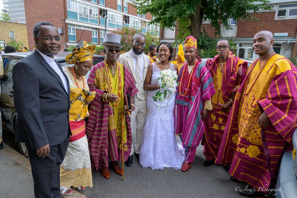 A wedding party in colorful traditional African attire with vibrant yellow and pink robes gathered outdoors.