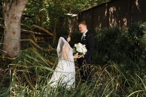 A bride and groom share a romantic moment in tall grass and trees during their outdoor wedding photoshoot.