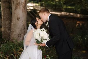 A romantic wedding couple embraces in a wooded outdoor setting while sharing an intimate moment together.