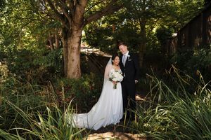A beautiful wedding couple embraces in an outdoor garden setting with lush greenery and natural lighting.