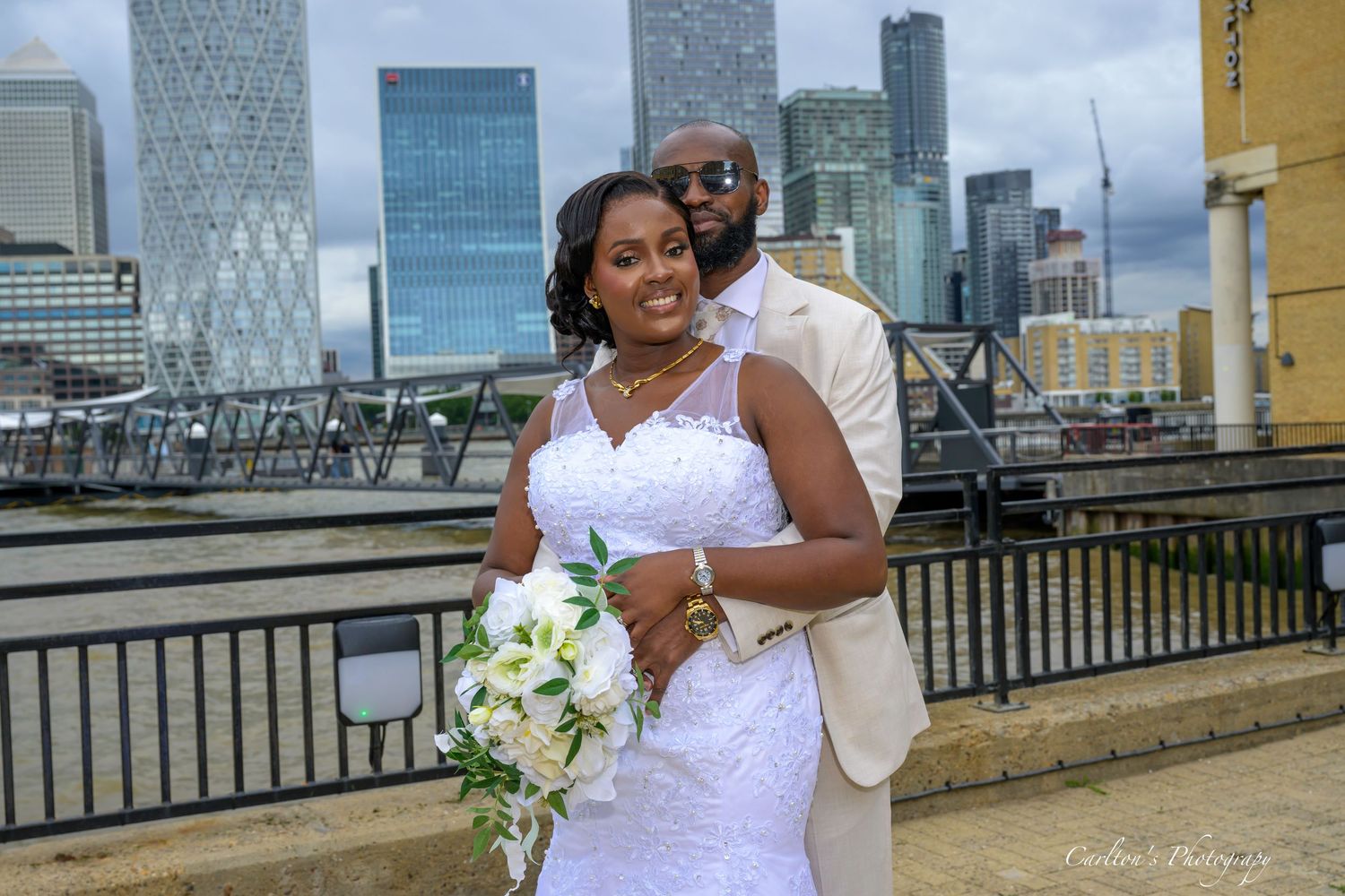 Wedding party in champagne bridesmaid dresses poses along waterfront with city skyline in background.