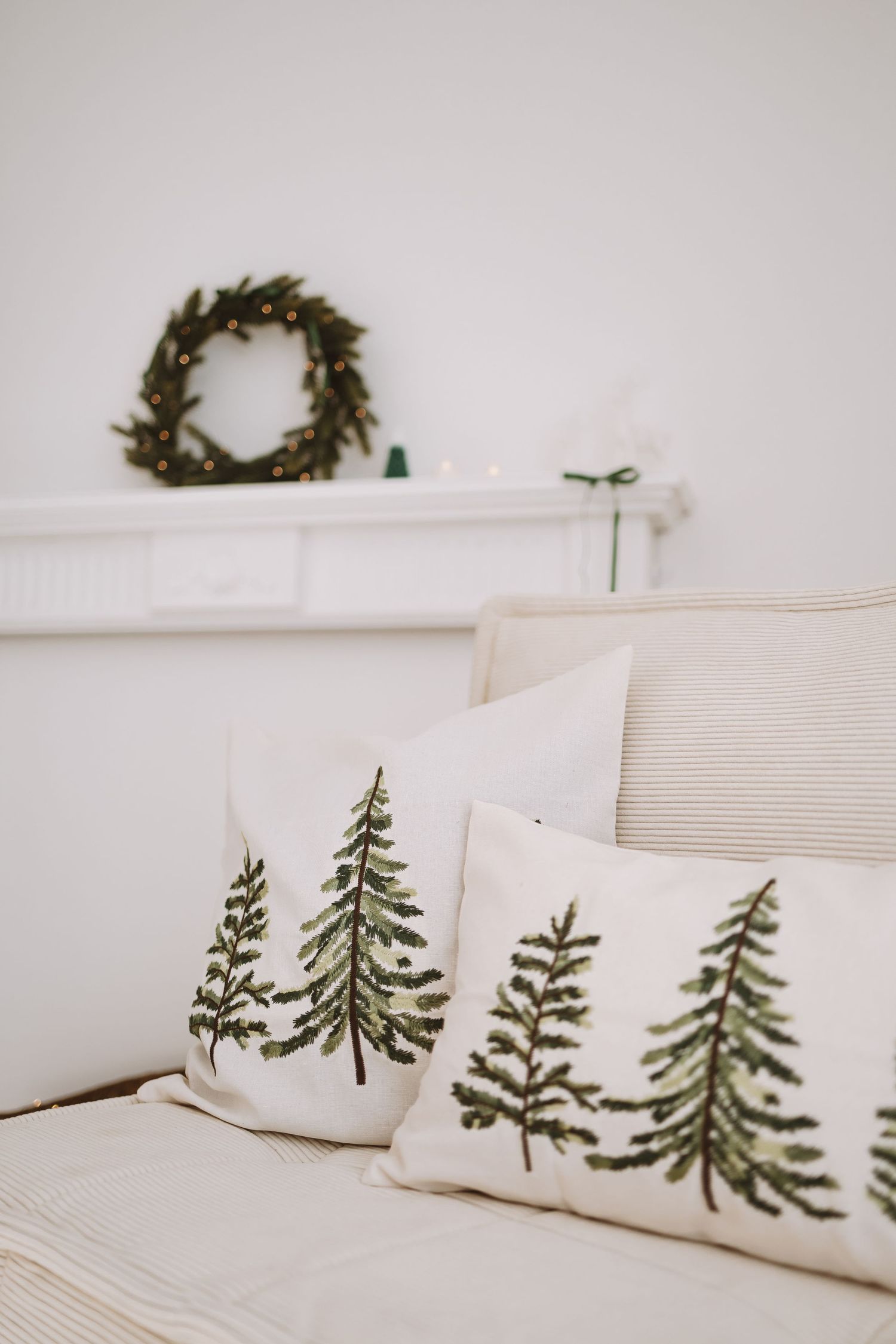 A series of four white bed pillows with embroidered green pine tree designs arranged on a minimalist white bed.
