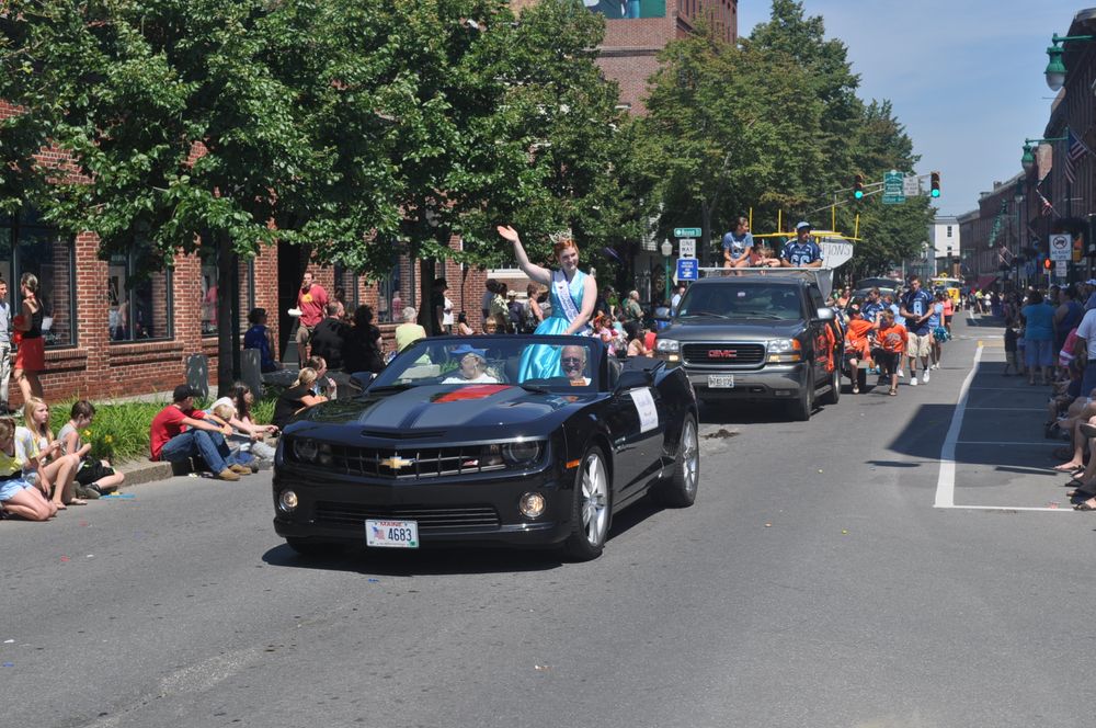 Vintage cars and spectators line a small town street during a parade or festival.