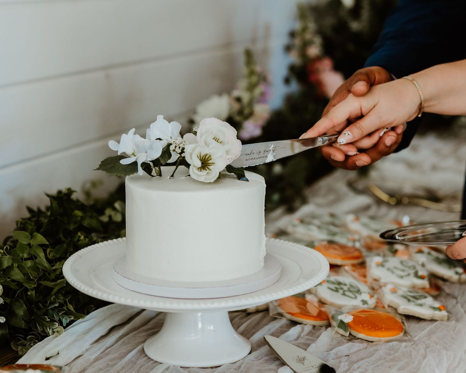 White wedding cake being cut with decorative flowers on wooden table.