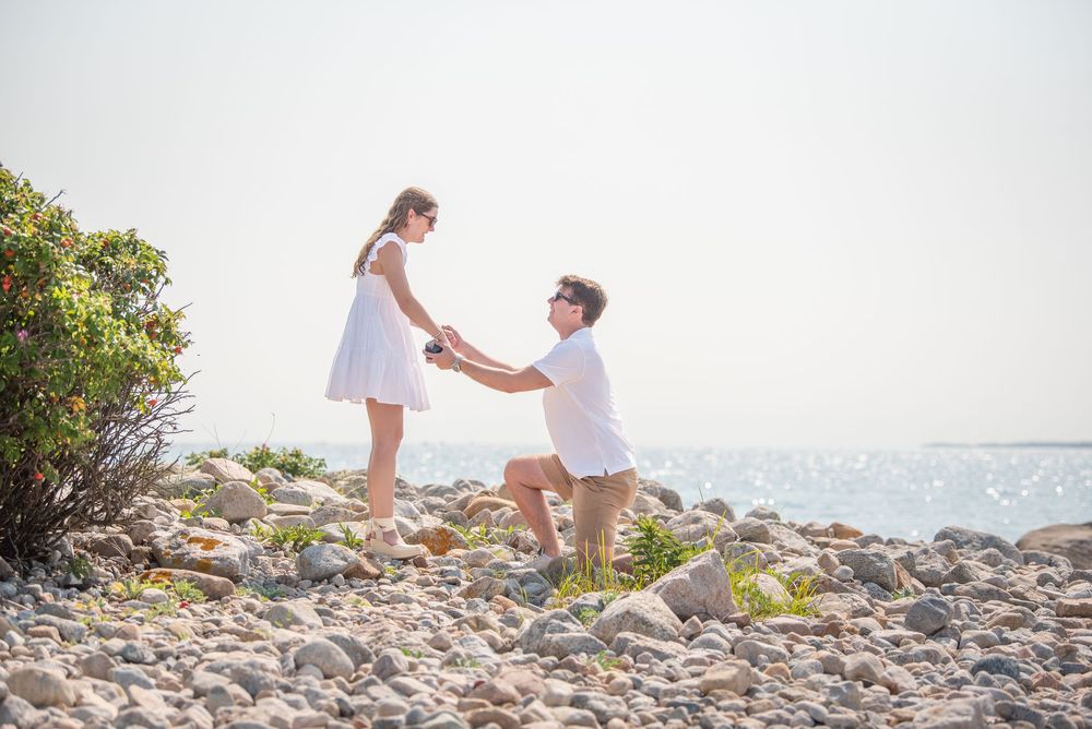 Romantic seaside proposal scene with couple on rocky beach.