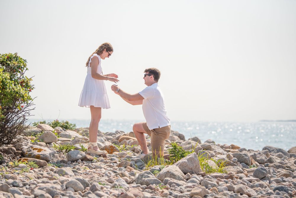 Marriage proposal unfolding on rocky coastal shoreline.