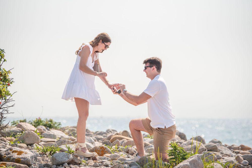 A romantic seaside proposal moment captured on a rocky beach during golden hour.