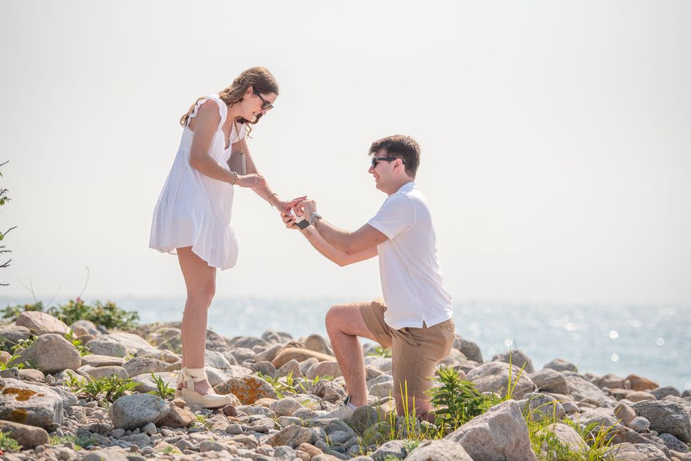 A couple sharing a special moment on a rocky coastal overlook in white summer attire.
