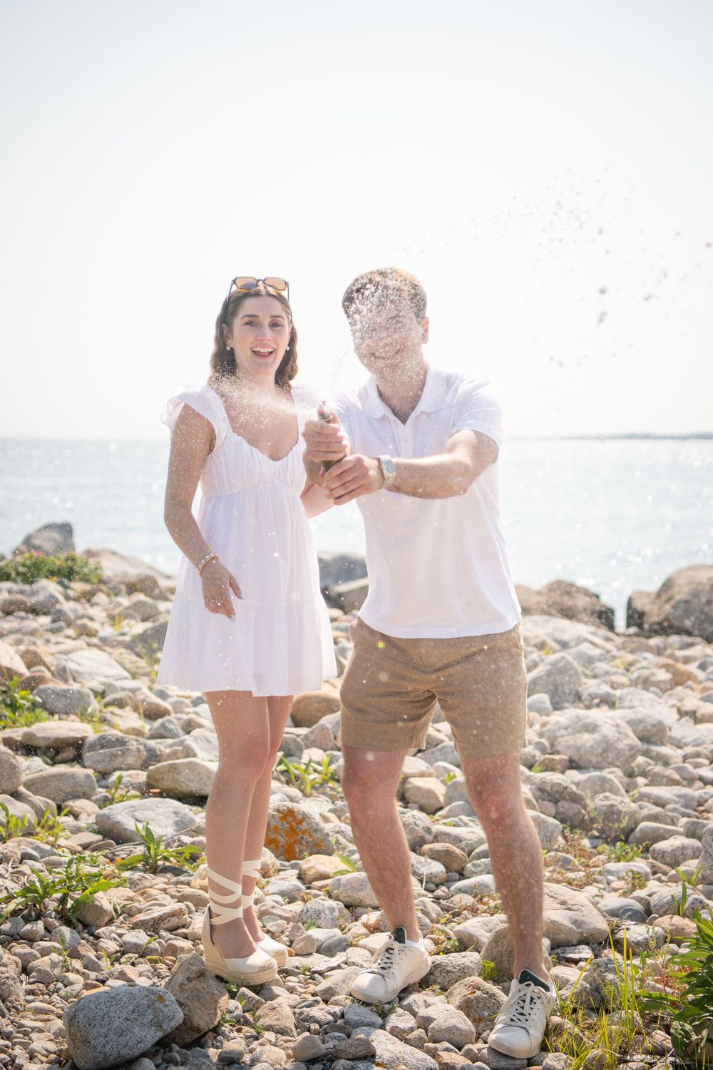 Happy couple laughing while playing with sand on a rocky beach.