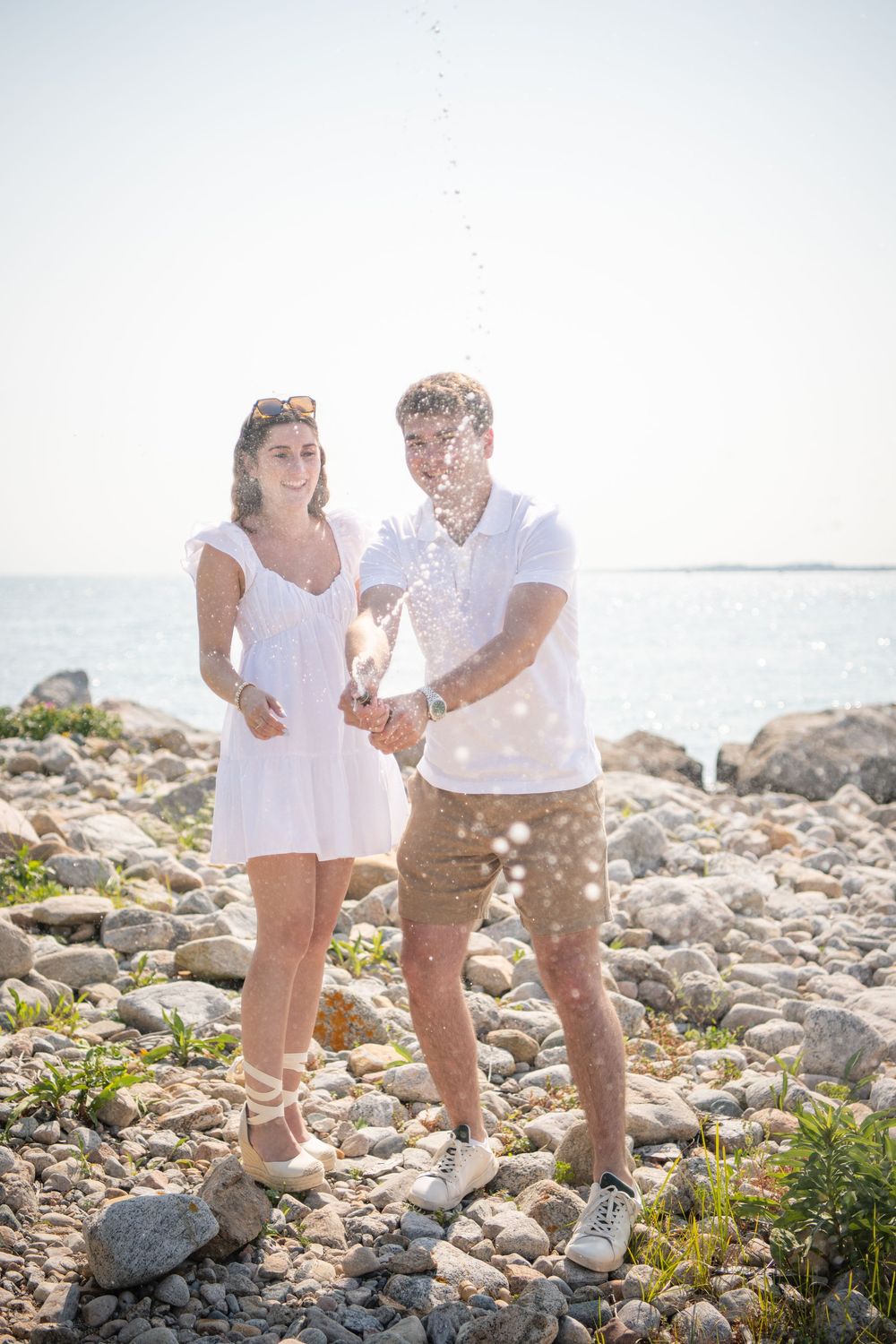 Playful beach engagement photoshoot with sand throwing and laughter.