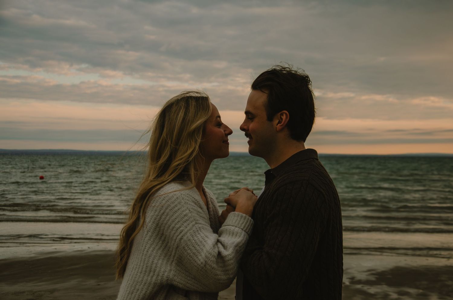 A silhouetted couple embraces on a moody beach at sunset with dramatic cloudy skies and ocean waves.