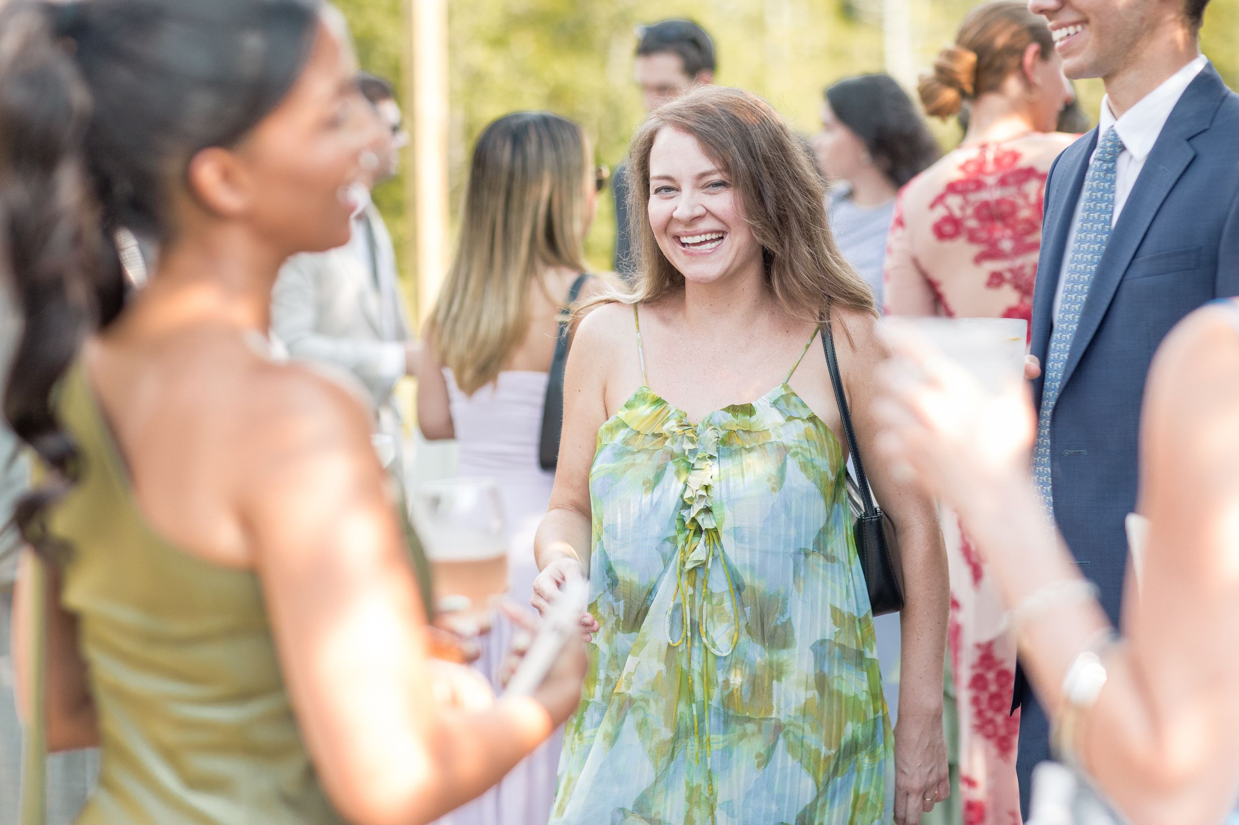 Wedding guests mingle and converse during an outdoor garden reception on a sunny afternoon.