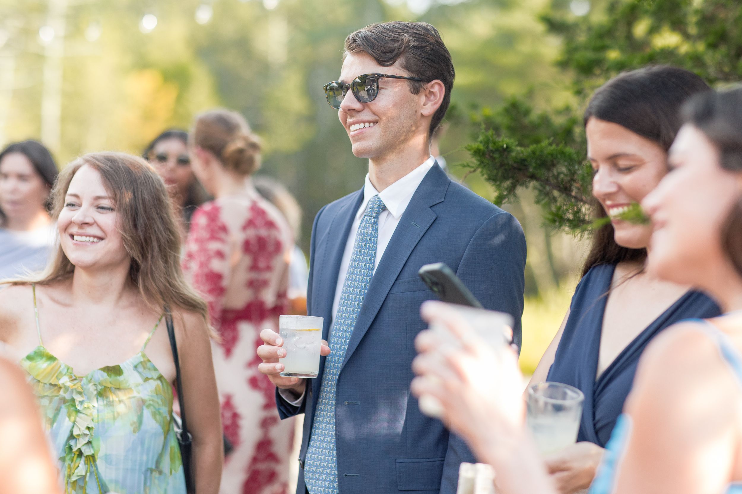 A crowd of wedding guests mingle and celebrate outdoors during a sunny garden reception.