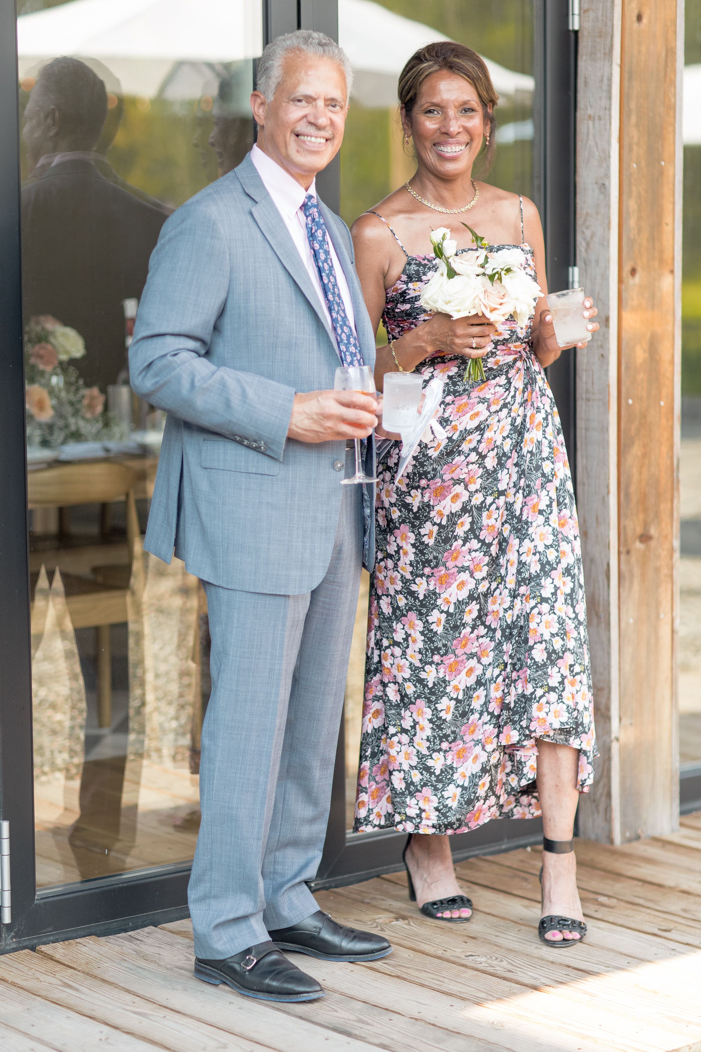 A couple in formal attire shares a joyful moment, with the man in a gray suit and woman in a floral dress.