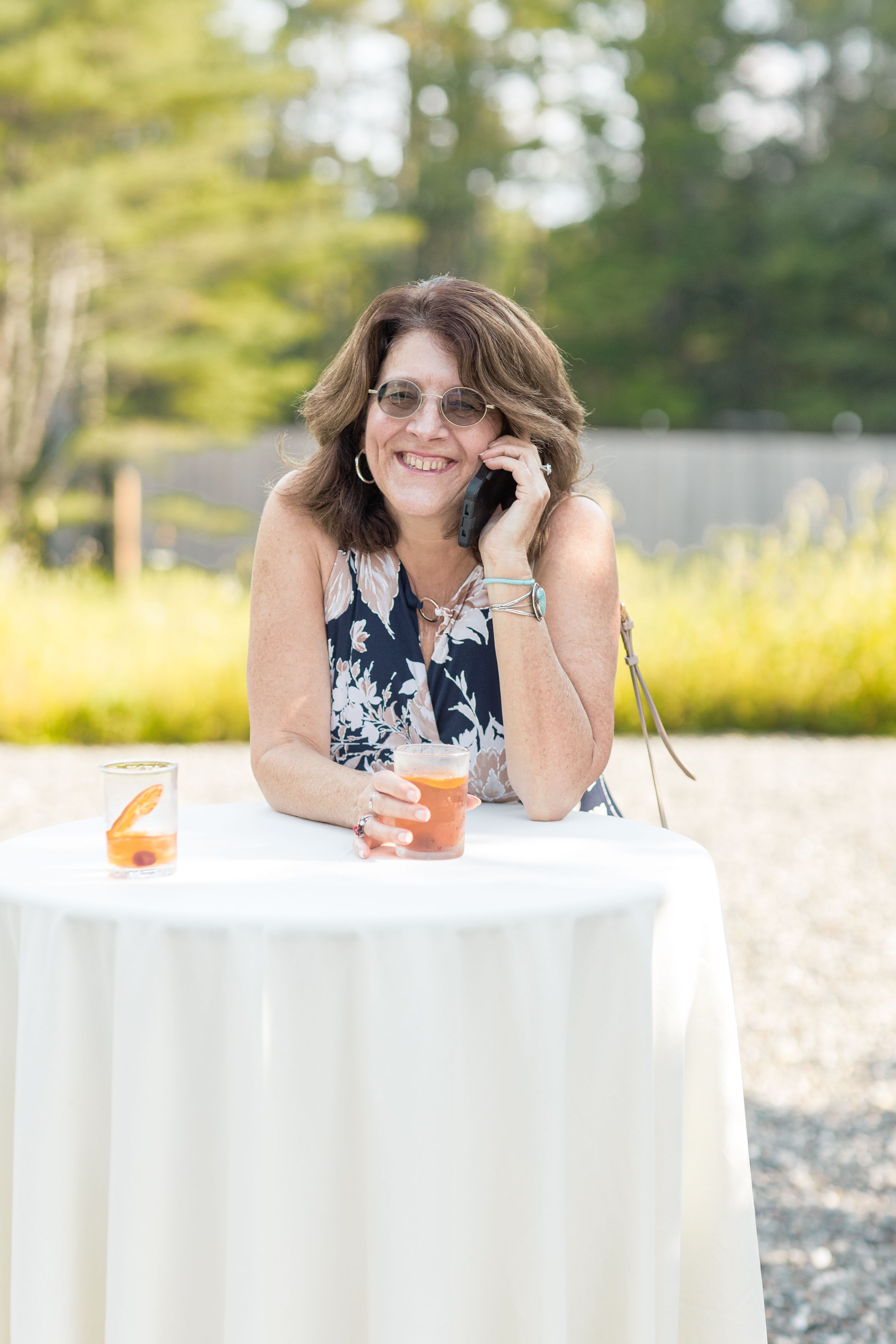 Person in navy and white dress lying relaxed on white linens at an outdoor table setting with trees in background.