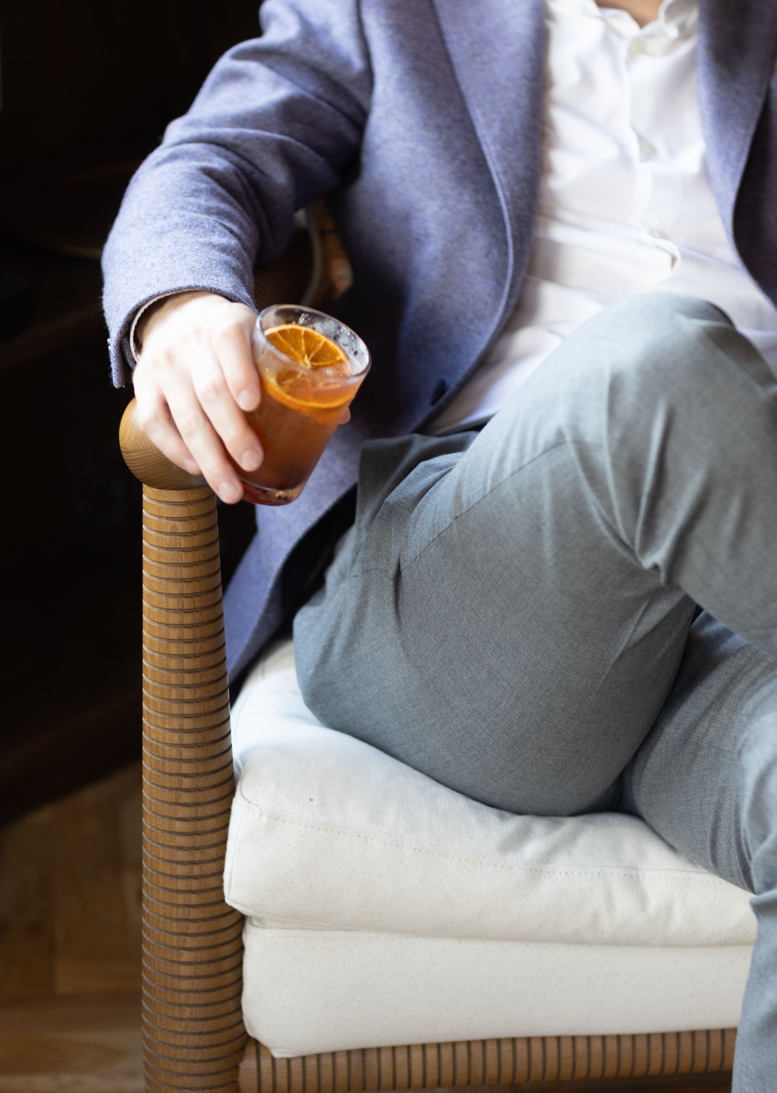 Person relaxing in wicker chair holding amber-colored cocktail or beer in glass on armrest.