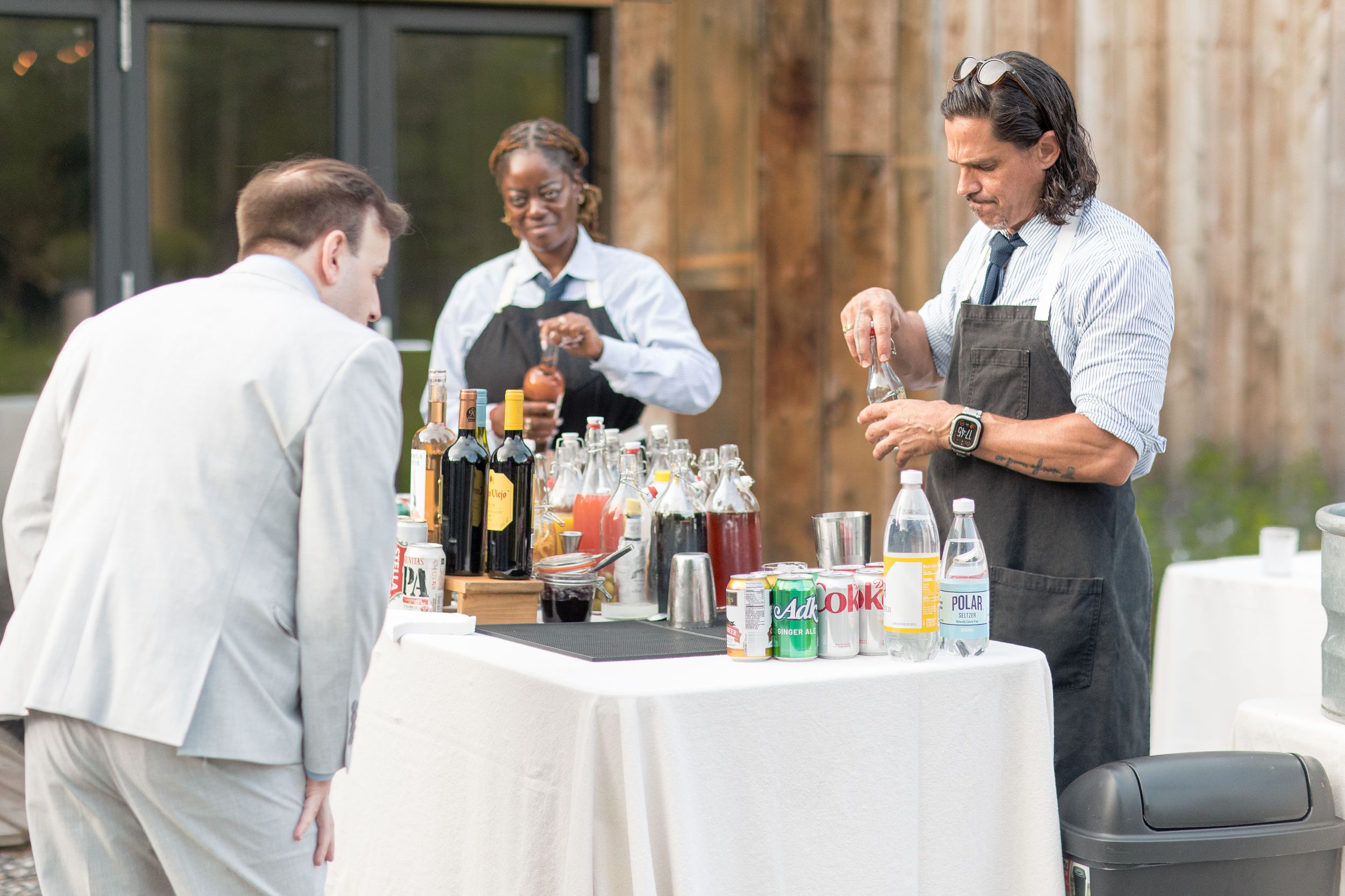 A bar setup at an outdoor event with bartenders serving drinks to guests at a rustic wood venue.