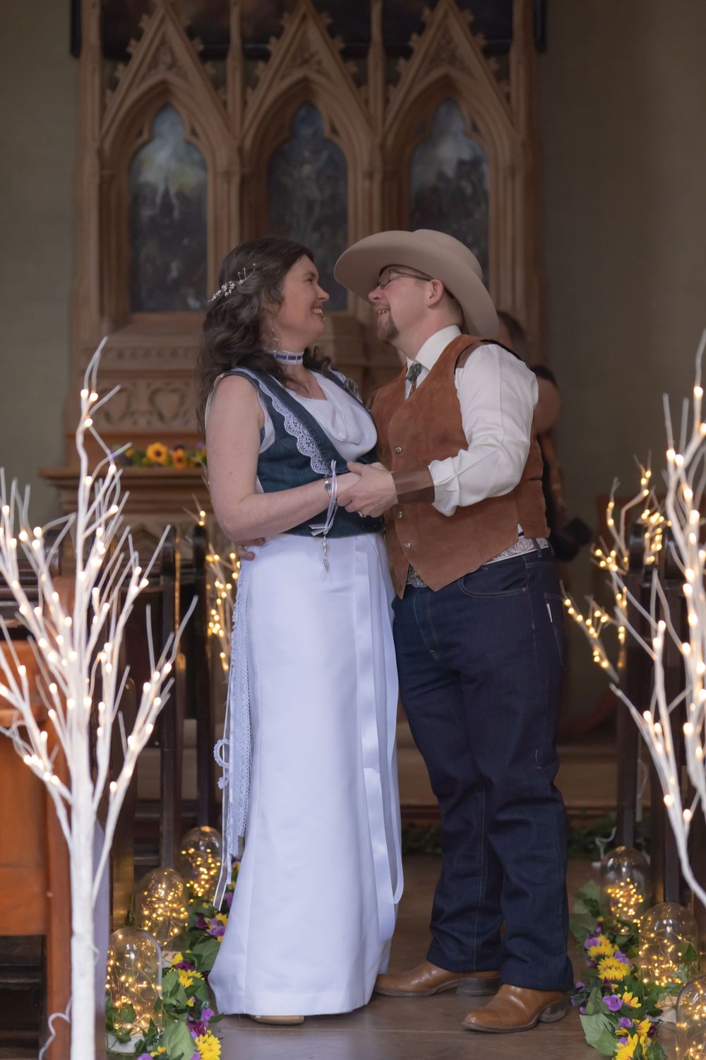 A couple shares a romantic dance with illuminated branches and flowers decorating an indoor church or chapel setting.