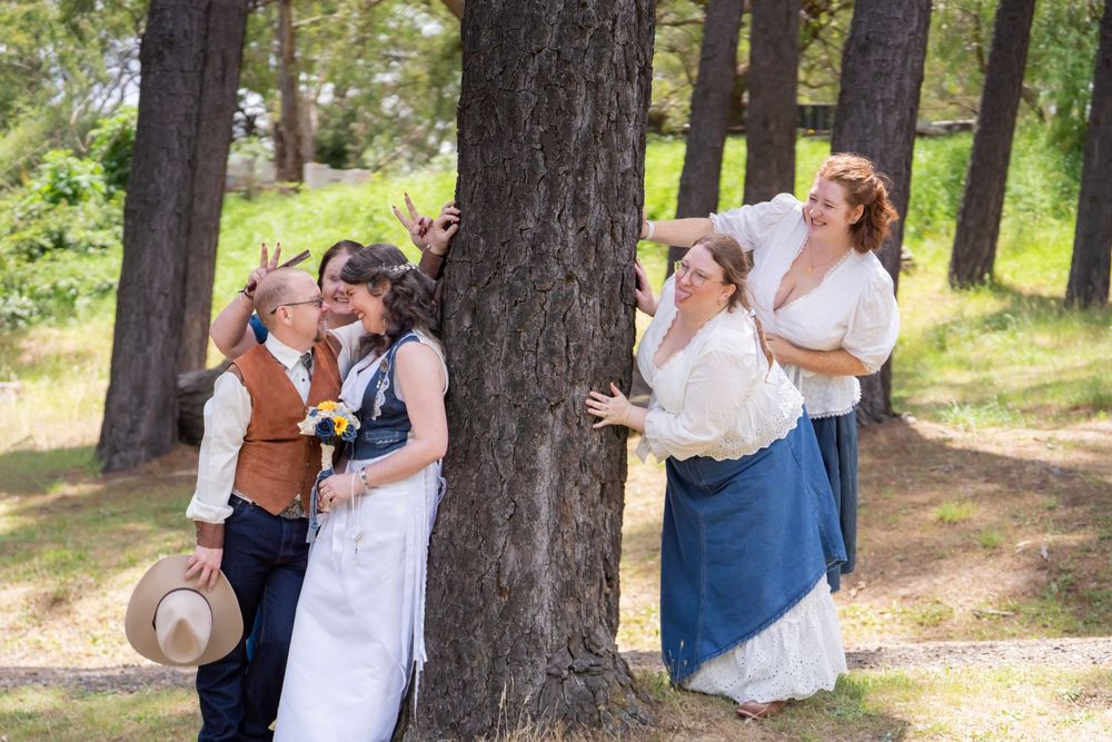 A couples photoshoot in a forest with two pairs standing against trees and embracing in casual wedding attire.