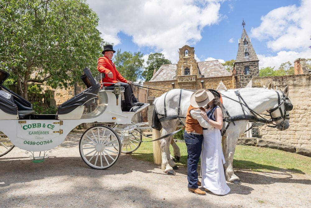 A white horse-drawn carriage with driver stands outside a historic stone church building on a sunny day.