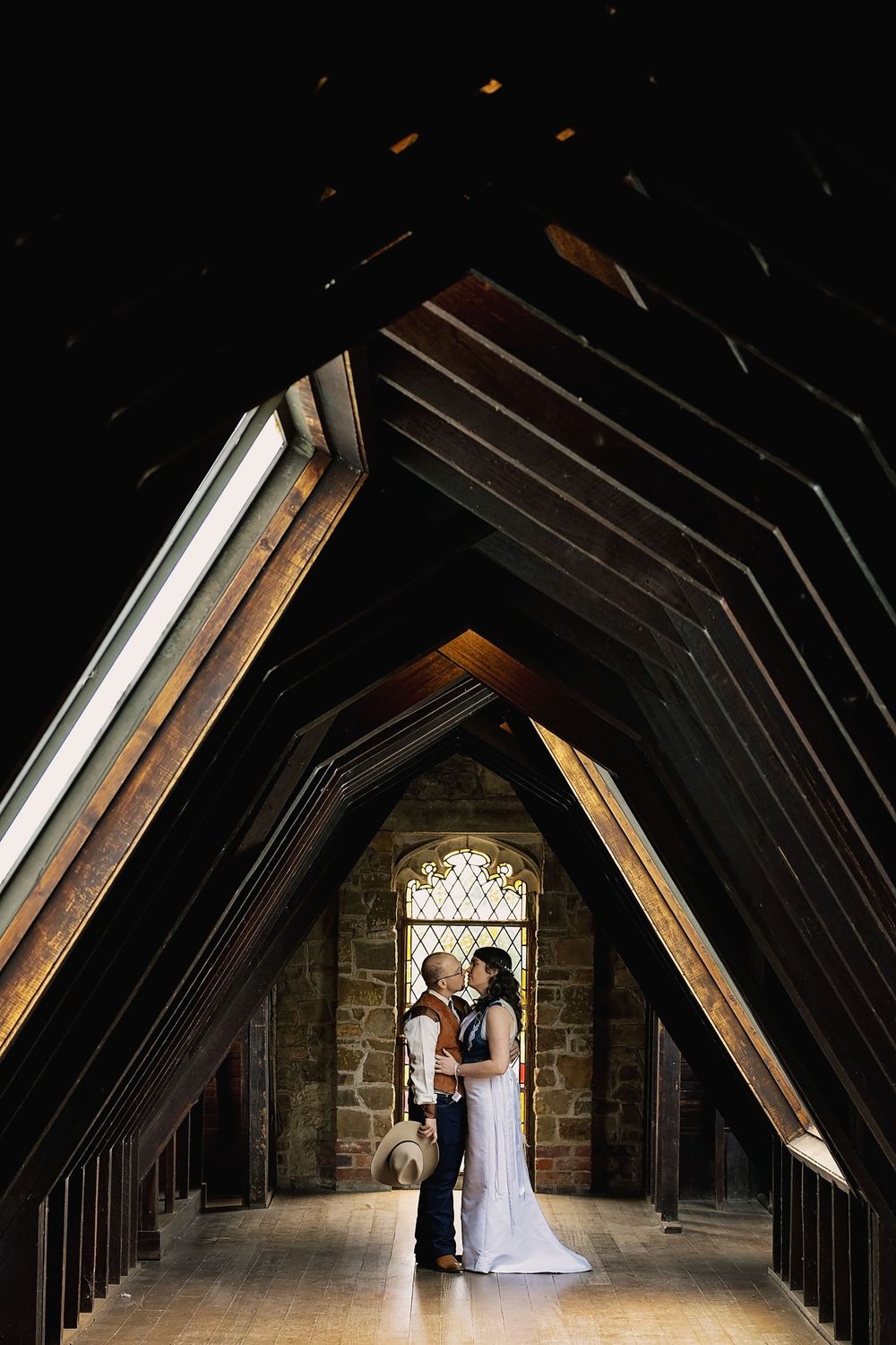 A dramatic architectural shot of a Gothic cathedral's wooden beam attic with arched window and stone walls.
