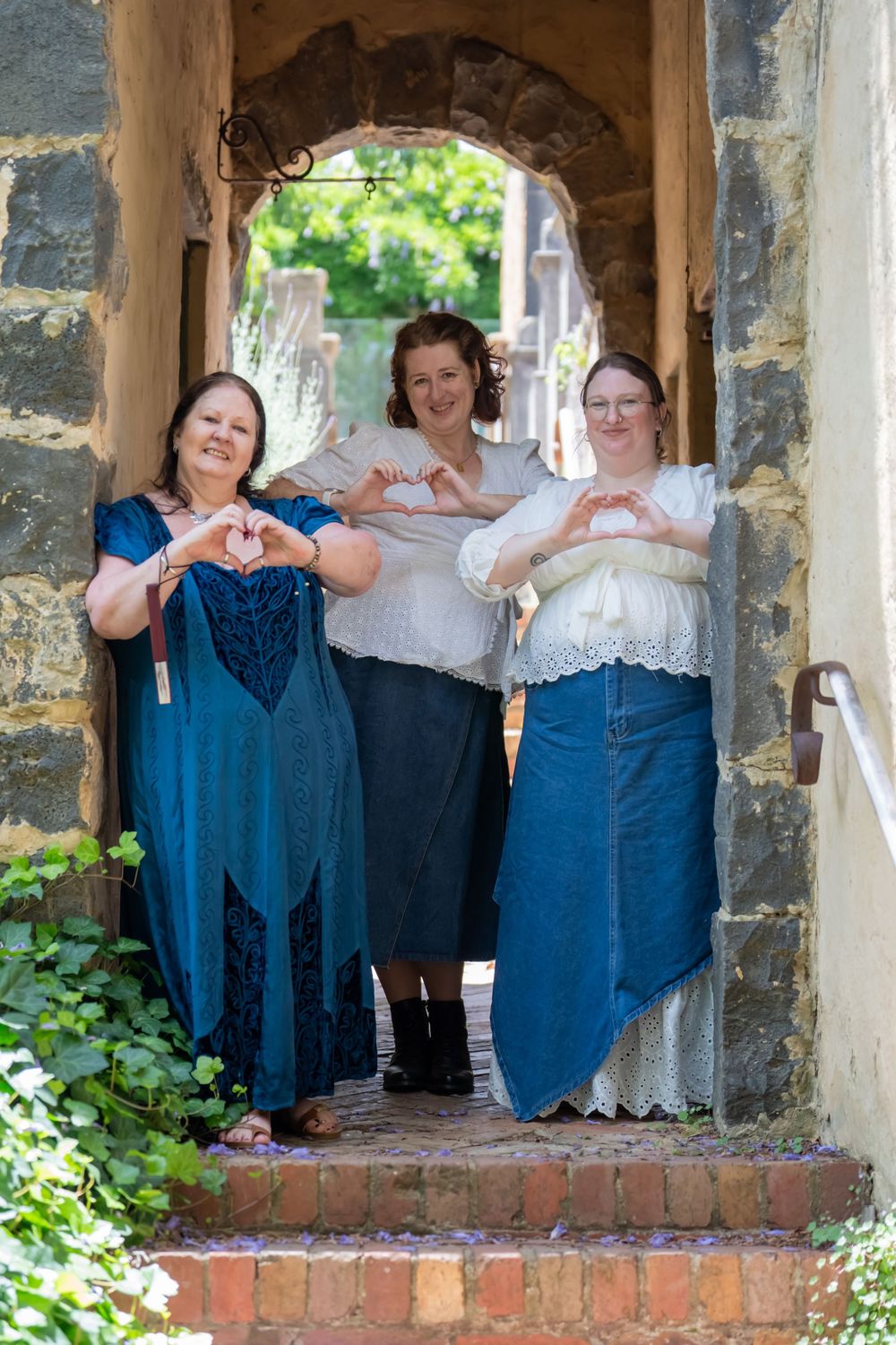 A group makes heart shapes with their hands while posing in a stone archway with blue and white attire.